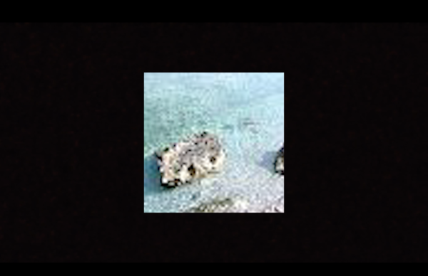 A film still: Inside a huge black frame, an image of a rock in the middle of a turquoise beach